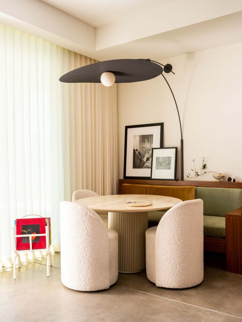 Round travertine dining table with bouclé chairs beneath a sweeping black arc lamp