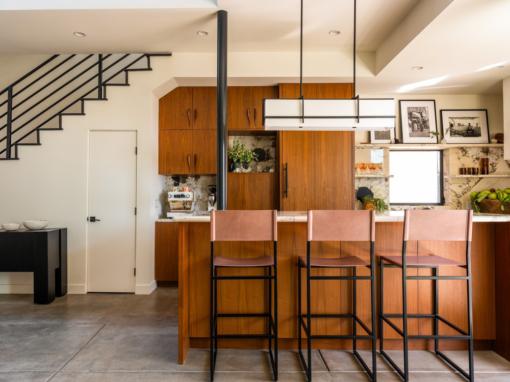 Walnut kitchen island with three leather bar stools and framed black and white photographs